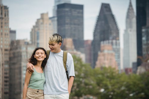 高兴的年轻民族夫妇拥抱而站在反对现代摩天大楼的风景秀丽的城市景观 · 免费素材图片
