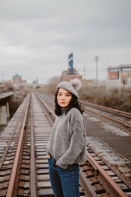 灰色针织毛衣和蓝色牛仔牛仔裤，站在火车铁轨上的女人 · 免费素材图片
