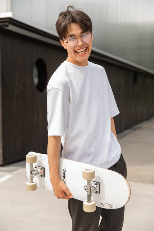 快乐的族裔男性少年携带滑板，在公园训练后笑 · 免费素材图片