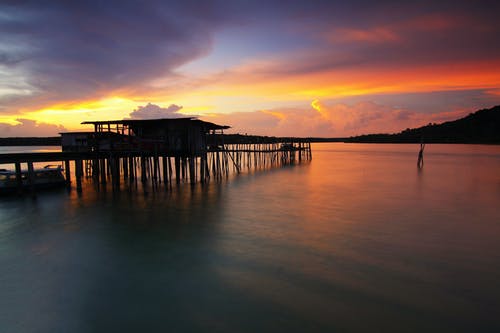 日落期间海上的木房子的轮廓 · 免费素材图片