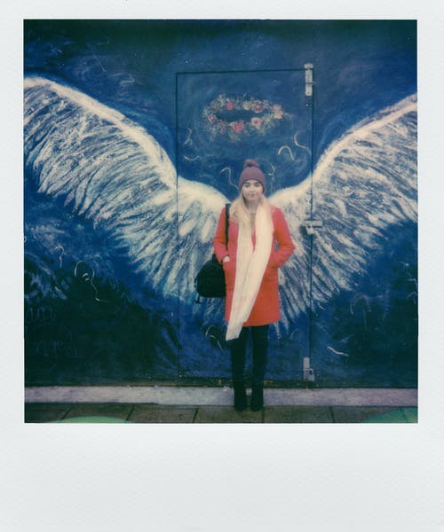 站在天使的翅膀前的橙色外套的女人 · 免费素材图片