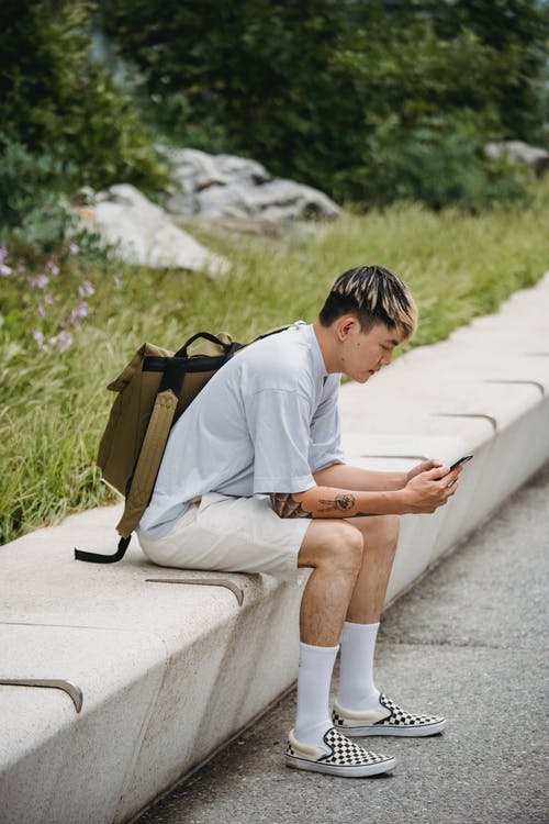 时髦年轻的族裔家伙在公园的长凳上休息，使用智能手机 · 免费素材图片