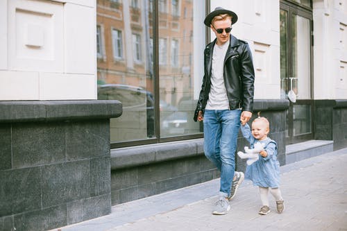 黑色西装外套和蓝色牛仔牛仔裤的男人抱着婴儿的蓝色牛仔牛仔裤手 · 免费素材图片