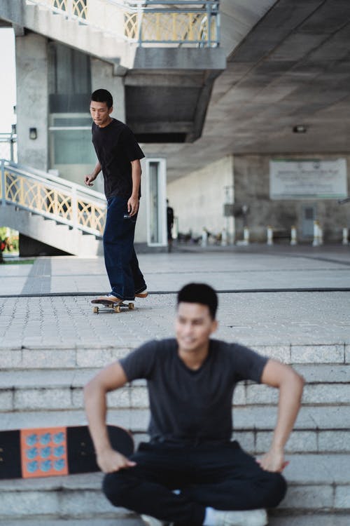 在休息的朋友附近的街道上的亚洲人骑马滑板 · 免费素材图片