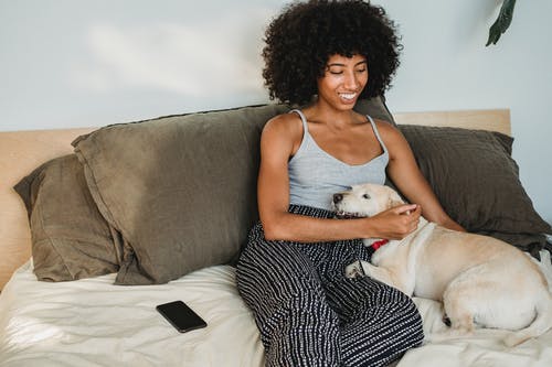 性格开朗的黑人妇女，在舒适的床上抚摸狗 · 免费素材图片