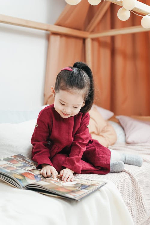 坐在床上看书的红裙子的女孩 · 免费素材图片