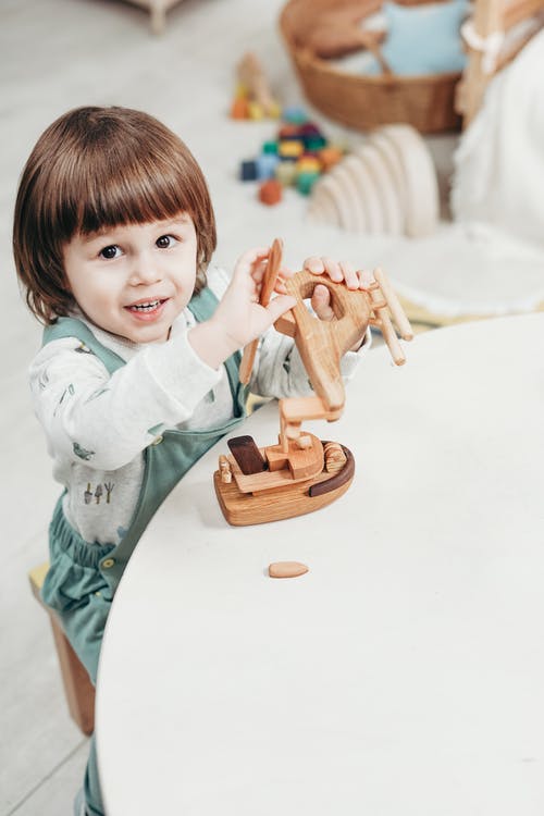 白色长袖上衣的孩子玩棕色木制玩具 · 免费素材图片