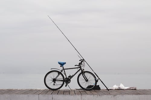 钓鱼竿和水泥地面上的黑色自行车 · 免费素材图片