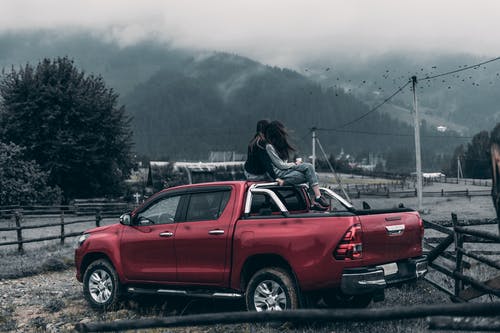 两个女人坐在红色的皮卡车上观看有雾的日子山 · 免费素材图片