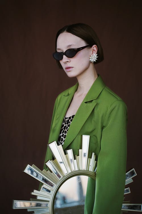 女人拿着阳光的墙镜时，戴着墨镜和绿色西装外套 · 免费素材图片