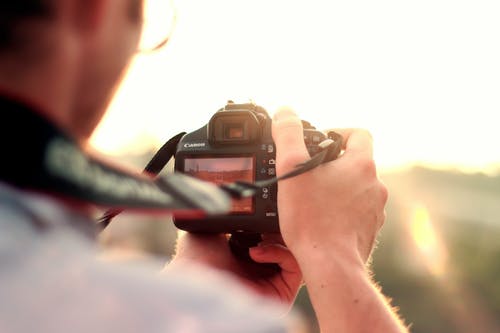 男子手持黑色单反相机站在太阳前 · 免费素材图片