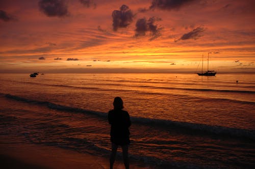 在日落时站在海边的人的身影 · 免费素材图片