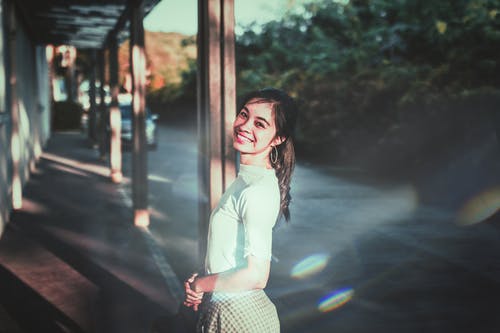 站在棕色的帖子旁边的白色上衣的微笑妇女 · 免费素材图片