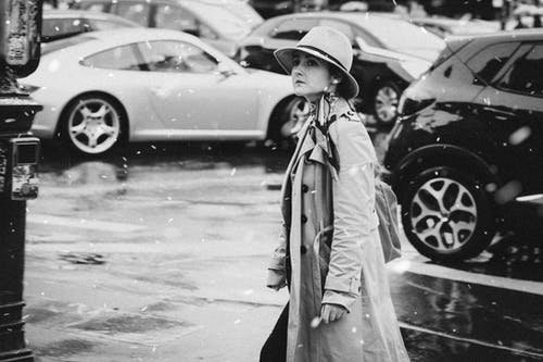 女人戴着帽子和外套站在车旁的灰度照片 · 免费素材图片