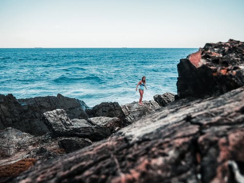 女人站在海边的岩石上 · 免费素材图片
