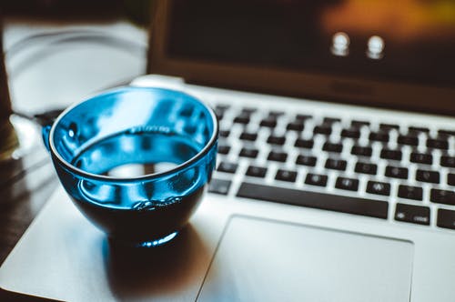 银色笔记本计算机上的蓝色玻璃杯的浅焦点摄影 · 免费素材图片