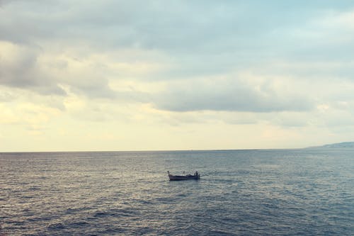 多云的白天天空在平静的水面上水上的木船 · 免费素材图片