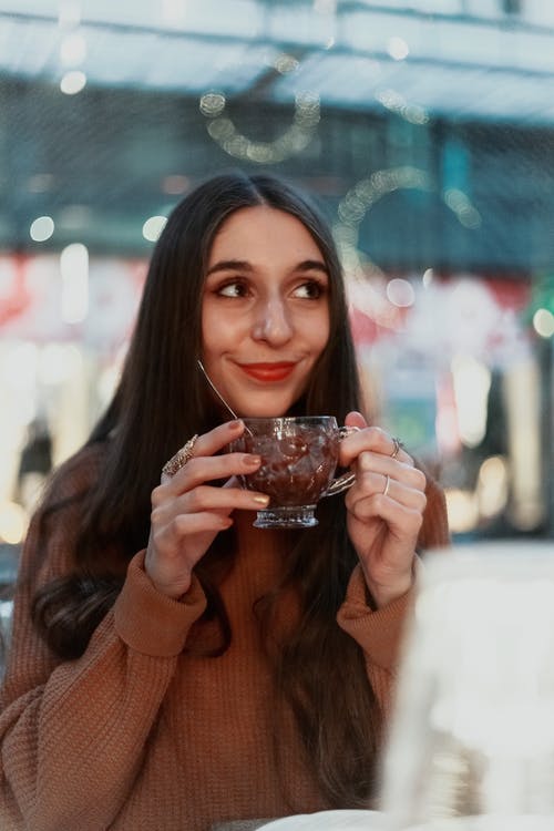 拿着杯子的时候穿棕色针织毛衫的女人 · 免费素材图片