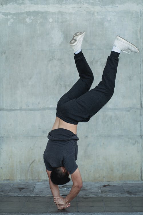 年轻运动员练习站在混凝土墙上背景的手上 · 免费素材图片