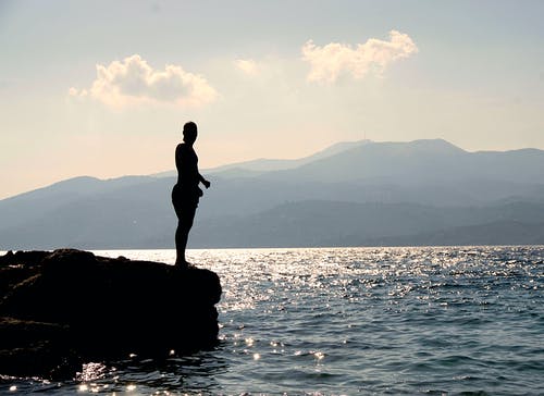 白天站在岛附近海面以外的岩石上的人 · 免费素材图片