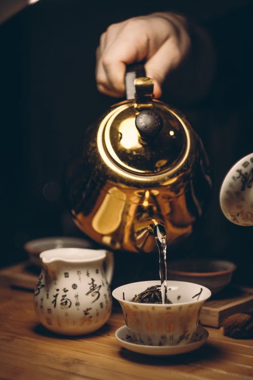 拿着金茶壶的人倒白色陶瓷茶杯 · 免费素材图片