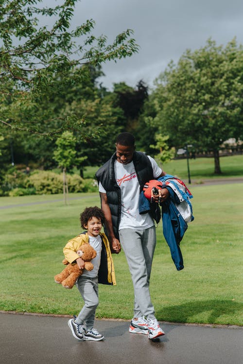 黑人与快乐的男孩，在公园附近的道路上行走 · 免费素材图片