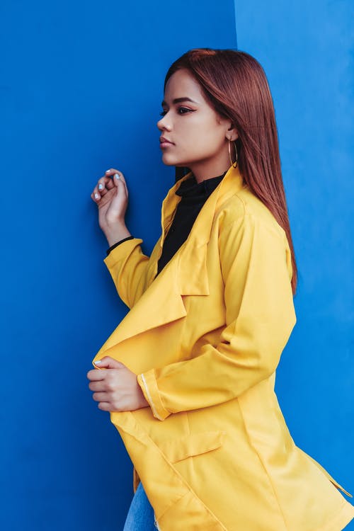 站在蓝色墙附近的黄色外套的女人 · 免费素材图片