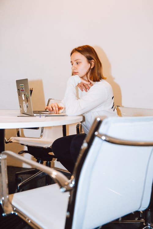 白色的长袖上衣，坐在椅子上在笔记本电脑上工作的女人 · 免费素材图片