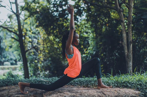 女人穿着橙色背心和黑色的裤子，在户外敲瑜伽姿势的照片 · 免费素材图片