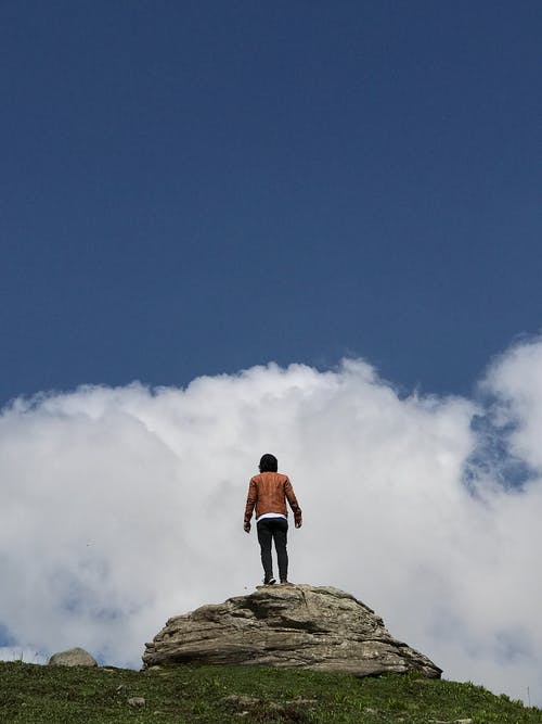 人站在一块岩石在蓝蓝的天空下 · 免费素材图片