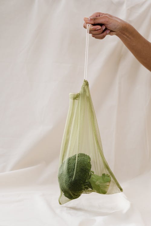 在绿色的塑料袋里拿着西兰花的人 · 免费素材图片