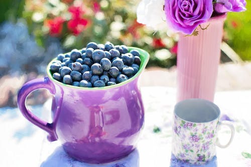 黑色浆果在白色和紫色花杯子旁边的紫色容器 · 免费素材图片