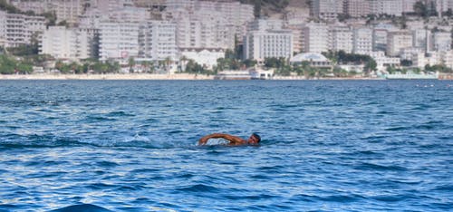 男子游泳在水白色混凝土高层建筑的背景中 · 免费素材图片