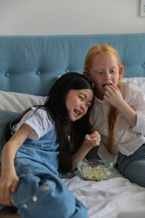 快乐的多样的女朋友在家里的床上吃爆米花 · 免费素材图片