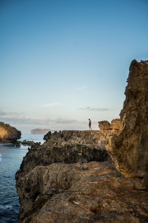 站在水体附近的岩层上的人 · 免费素材图片