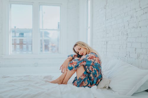 女人坐在床上穿花裙子 · 免费素材图片