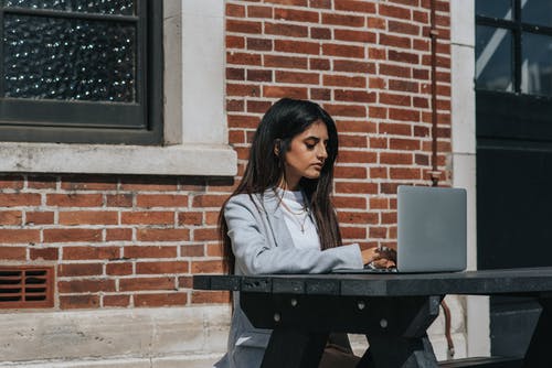 细心的族裔女性企业家在城里的笔记本电脑上打字 · 免费素材图片