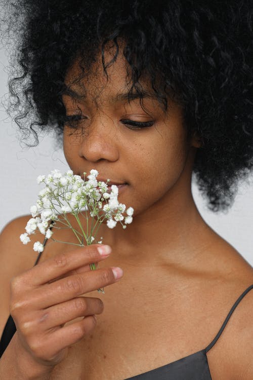 黑色意大利面条皮带顶部闻到白色花瓣花的女人的特写肖像照片 · 免费素材图片