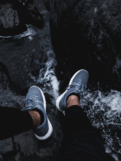 坐在岩石上的黑色裤子和灰色运动鞋的人 · 免费素材图片