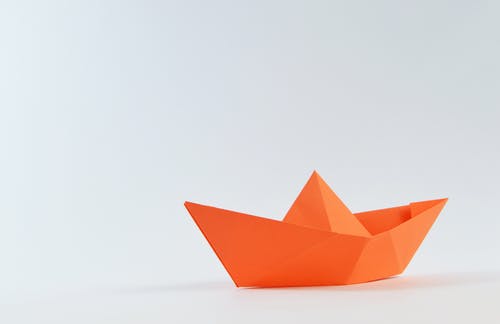 白色表面上的橙色纸船 · 免费素材图片