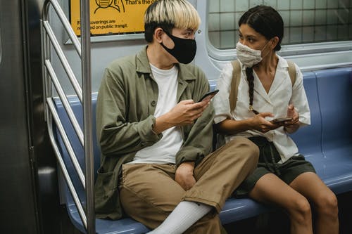 在医疗口罩骑火车和浏览智能手机的年轻多样夫妇 · 免费素材图片