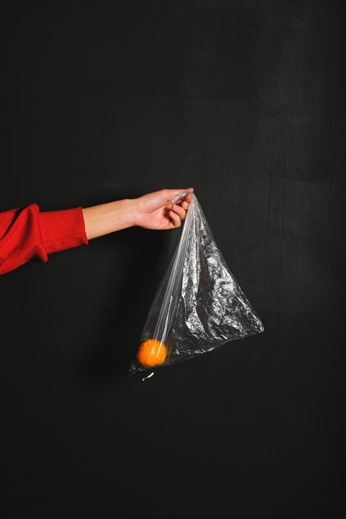拿着塑料袋与橙色的红色长袖衬衫的人 · 免费素材图片