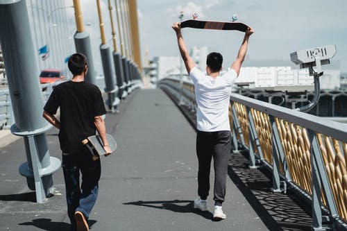 无法识别的滑板手在小镇的桥面人行道上行走 · 免费素材图片