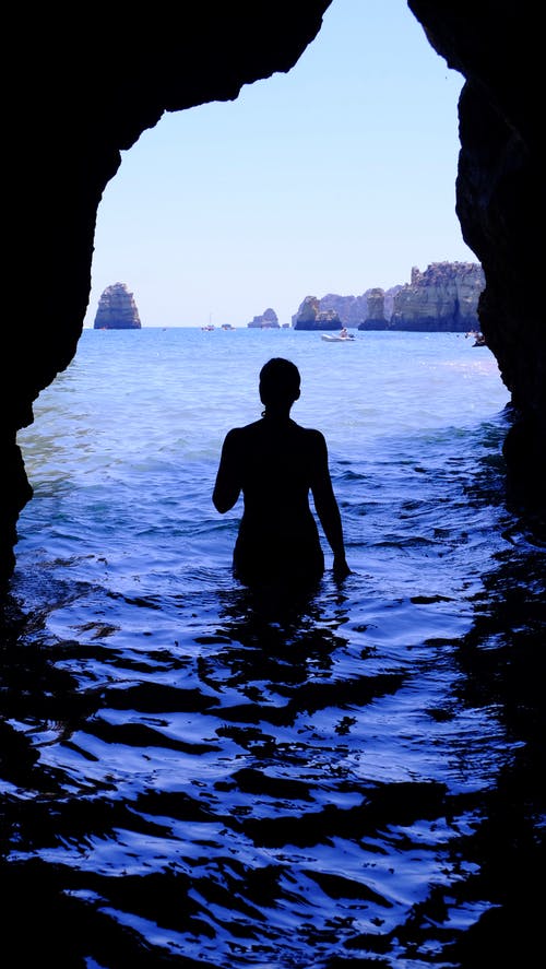 女人在白天黑洞内蓝色的大海中的剪影 · 免费素材图片
