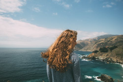 穿蓝色长袖衬衫站在悬崖附近海洋上的女人 · 免费素材图片