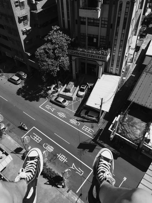 灰度摄影男子在街上和建筑物中穿着所有明星匡威高帮鞋 · 免费素材图片