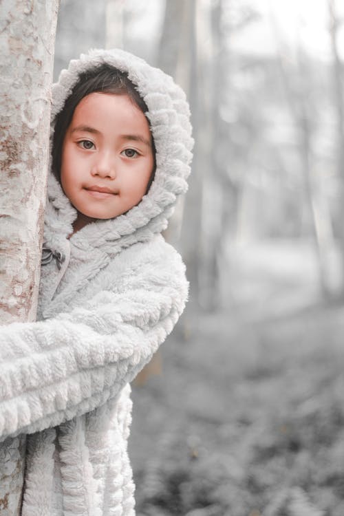 拥抱树干时穿雪夹克的女孩 · 免费素材图片