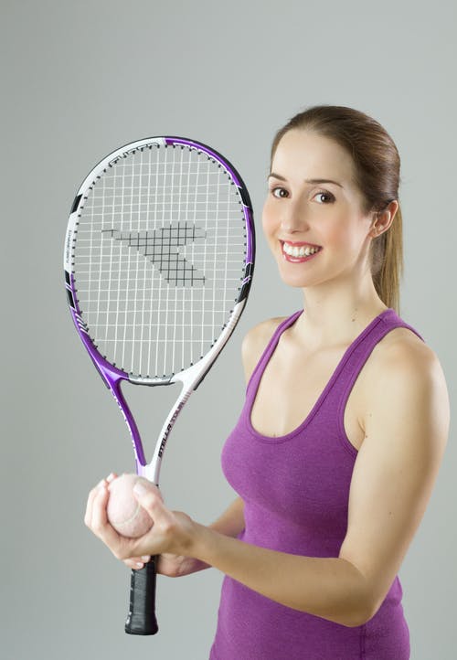 女人穿着紫色背心，拿着紫色和白色的球拍和草地网球球 · 免费素材图片