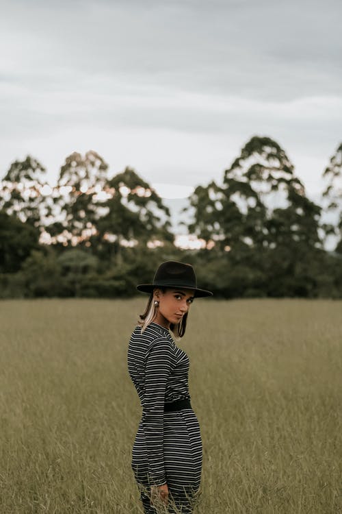 黑色和白色的条纹的长袖衬衫和黑色的帽子，站在绿色草地上的女人 · 免费素材图片