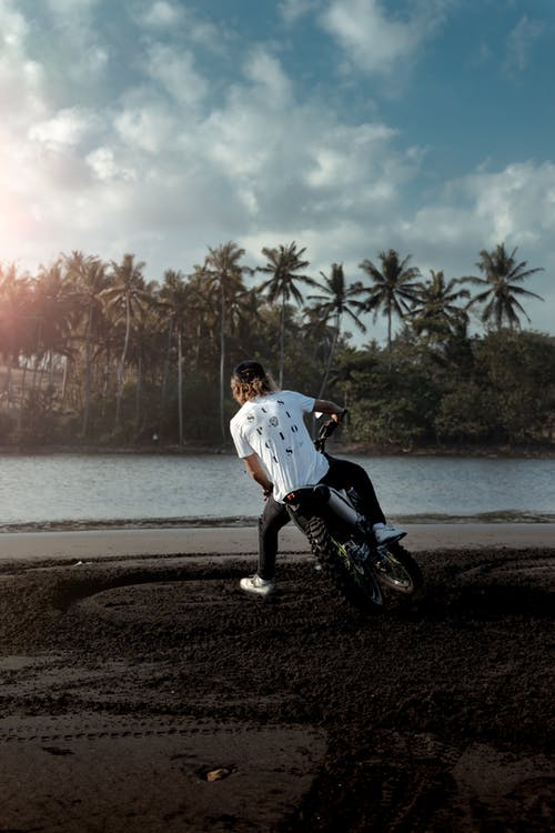 穿白衬衣骑摩托车在海滩上的人 · 免费素材图片